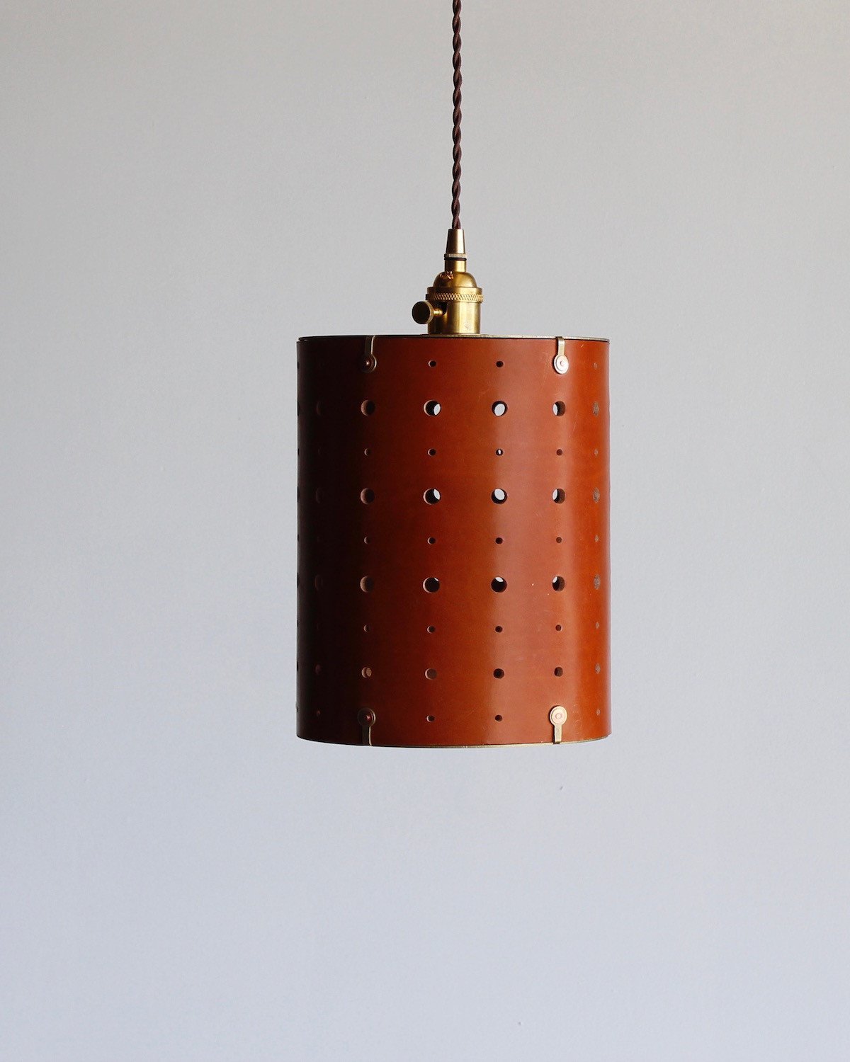 Tan leather cylinder pendant with handstitched, perforated leather shade. Made by Lostine in Philadelphia. Hardwired or plug light fixture. Simple interior design, made in the USA. #color_tan harness