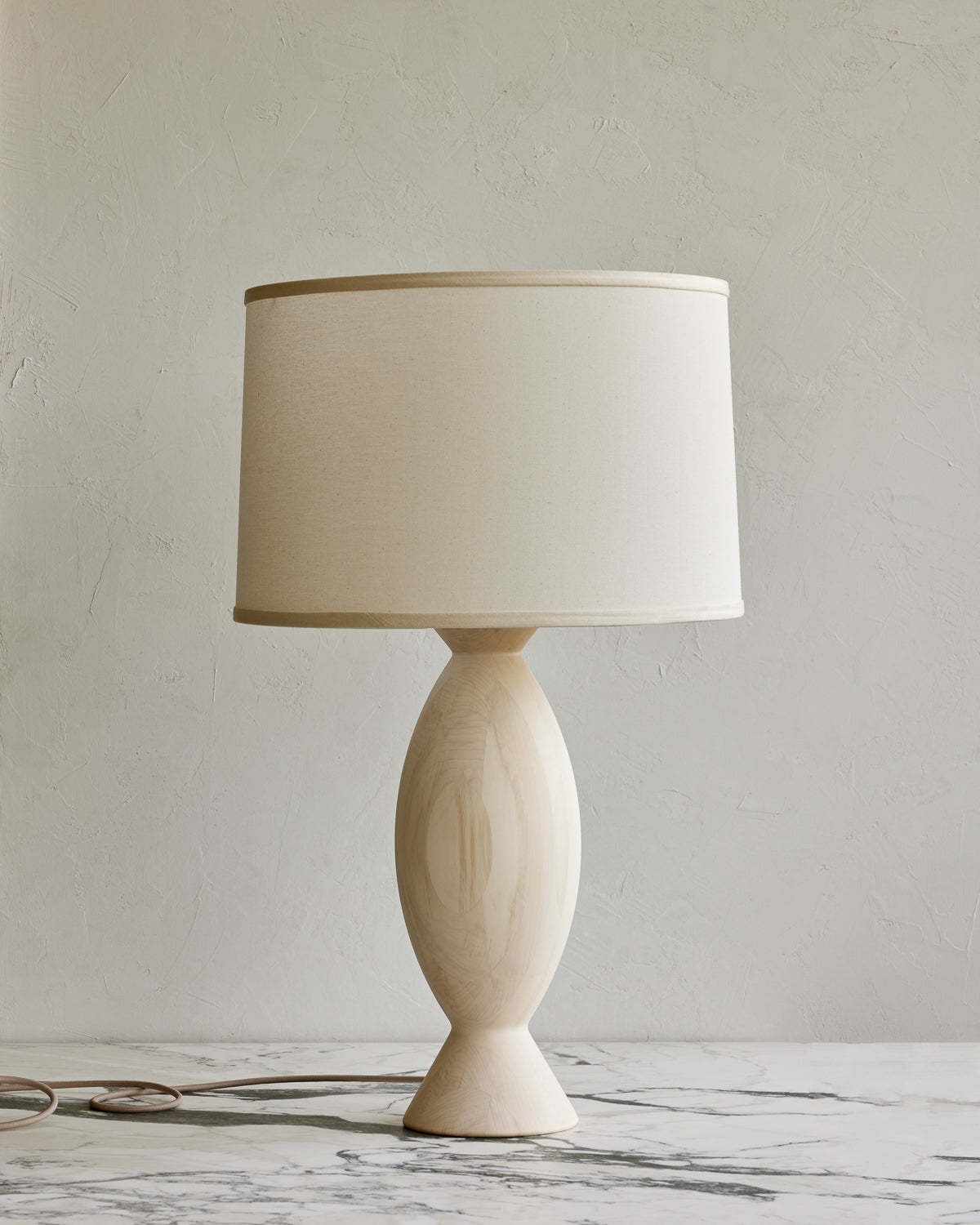 A traditional style table lamp with a round beige shade and a wooden base, possibly made of walnut or aspen wood. #wood-finish_aspen