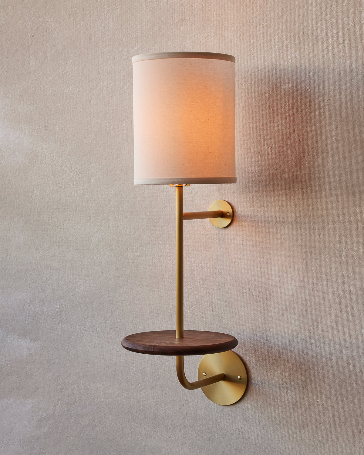 A wall-mounted sconce with a satin brass body, a textured natural Belgian linen shade, and a black walnut tray.