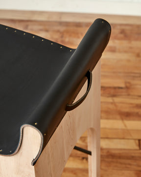 Sculpted stool with black leather and maple wooden base with metal foot rest and short backrest. Counter and bar height. Handmade in Philadelphia by Lostine. Simple Interior Design. Warm American Modern Design