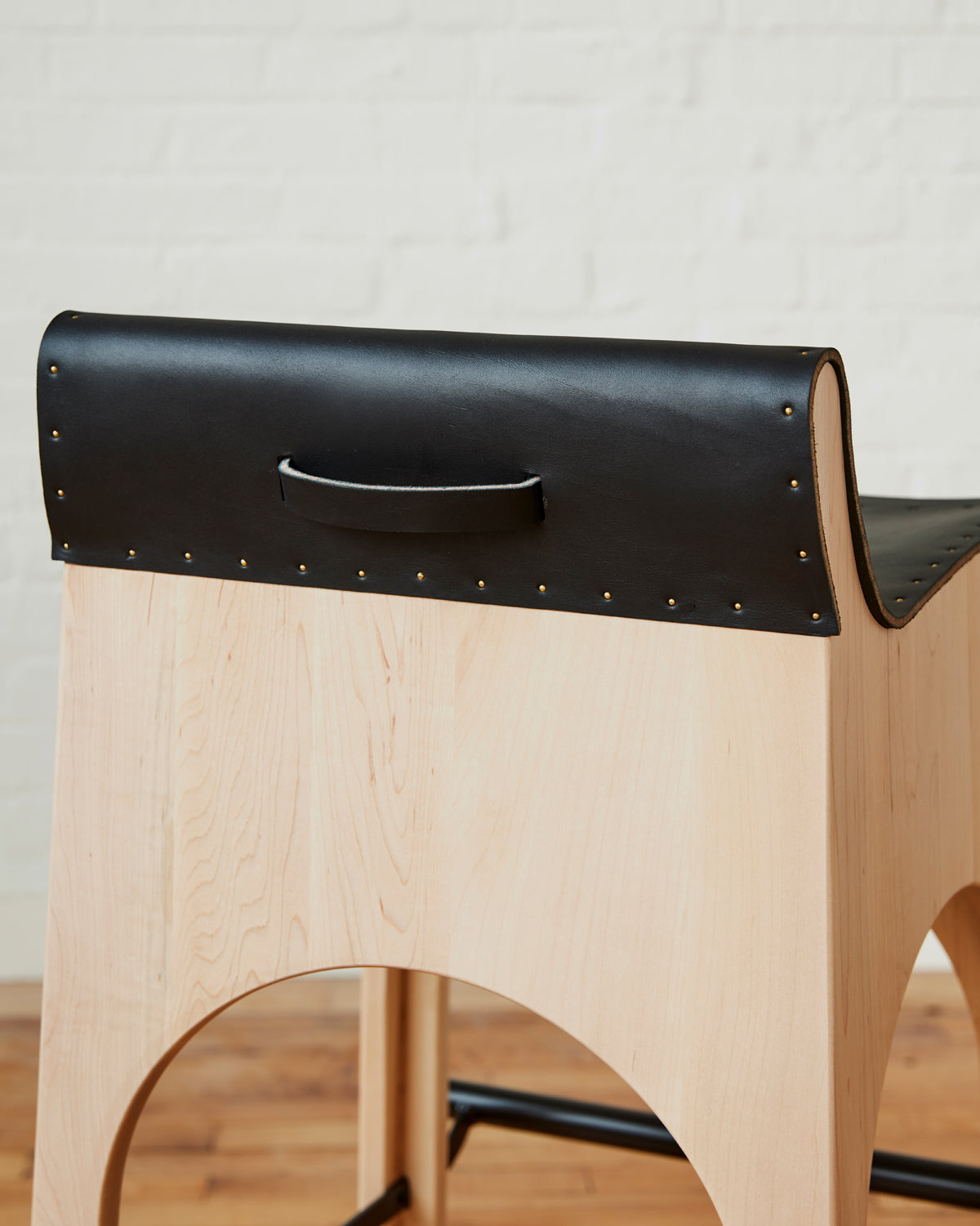 Sculpted stool with black leather and maple wooden base with metal foot rest and short backrest. Counter and bar height. Handmade in Philadelphia by Lostine. Simple Interior Design. Warm American Modern Design