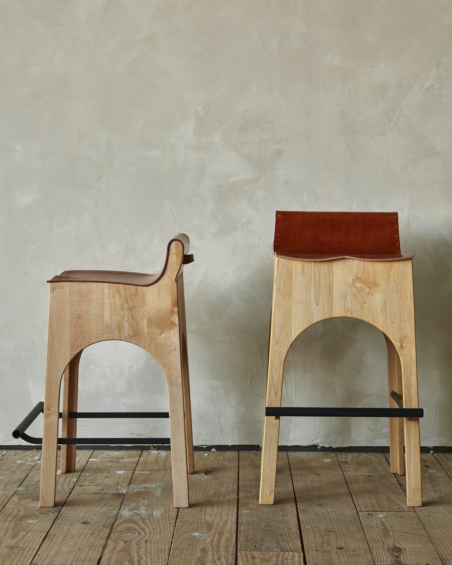 Sculpted stool with tan leather and maple wooden base with metal foot rest and short backrest. Counter and bar height. Handmade in Philadelphia by Lostine. Simple Interior Design. Warm American Modern Design